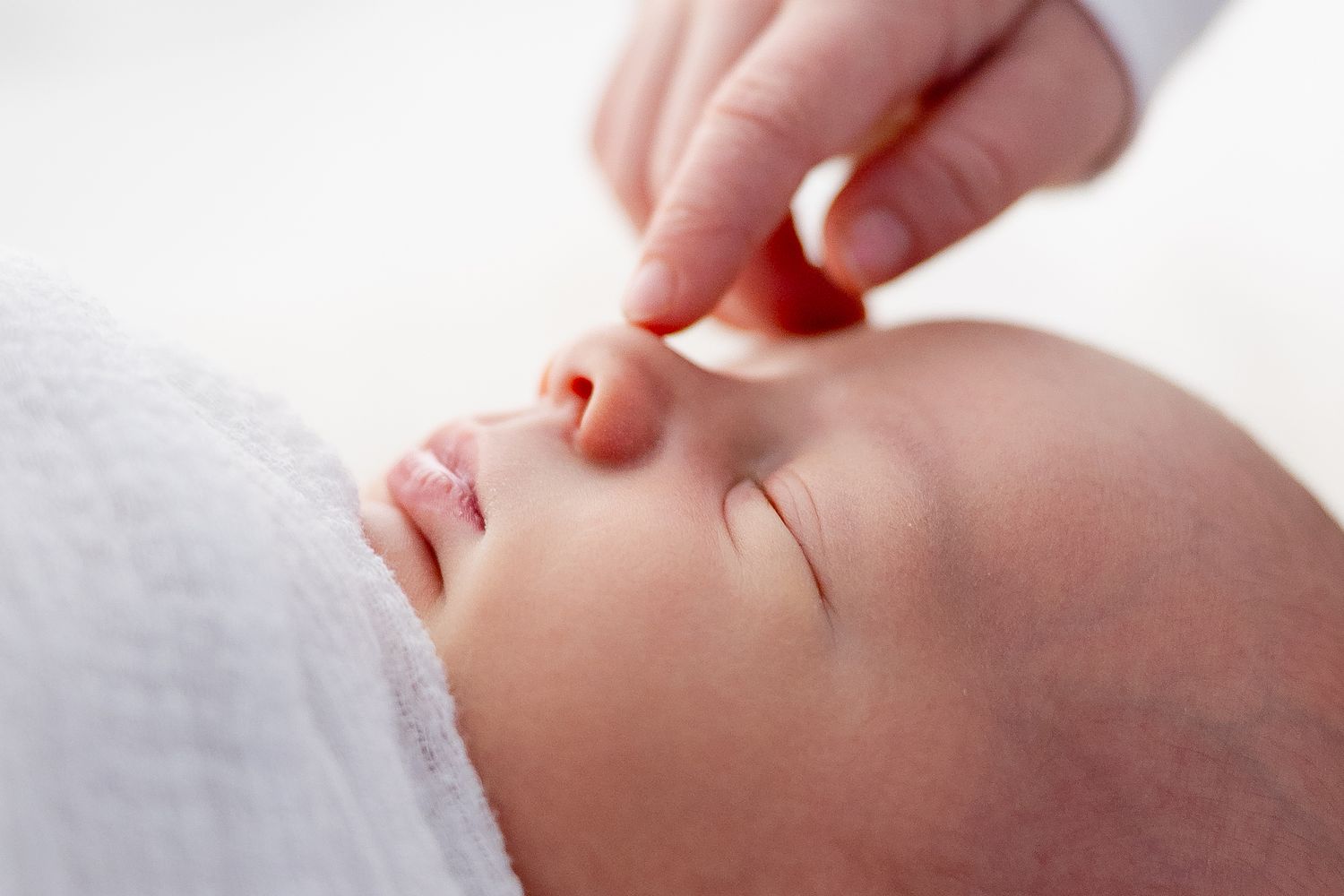 Gentle close-up profile of sleeping newborn baby against white background.