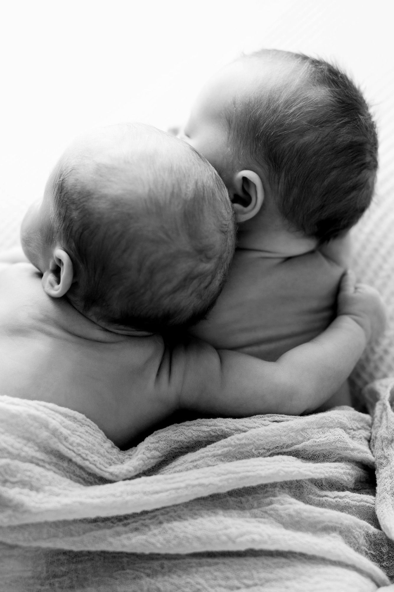 Two babies cuddling together in black and white portrait.
