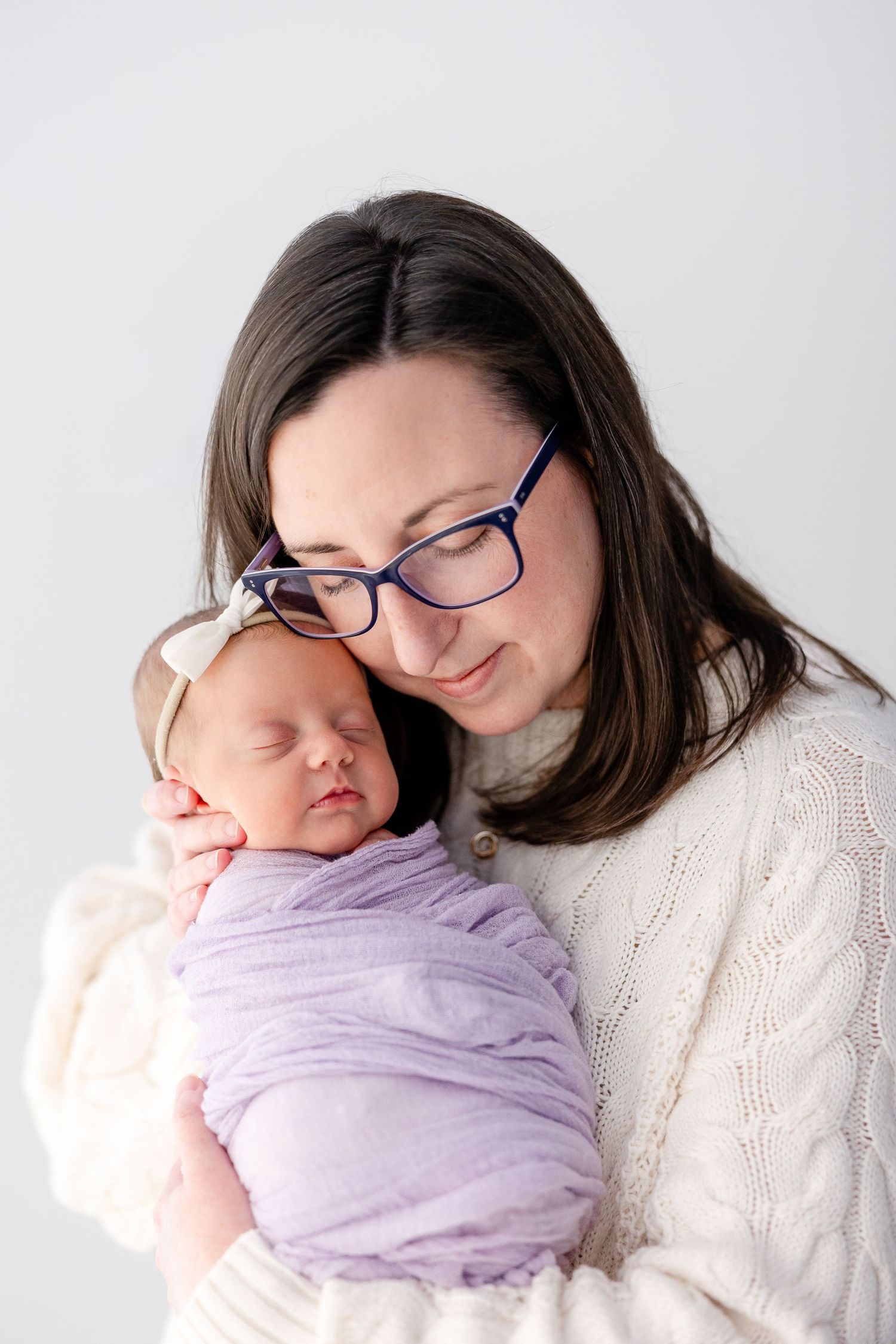 Tender moment captured in soft white and lavender tones showing parent and baby in matching cozy sweaters.