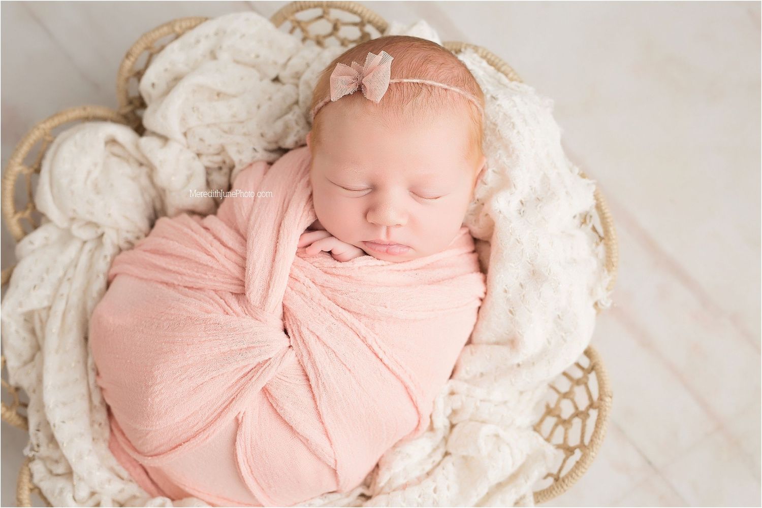 Newborn baby wrapped in soft pink swaddle blanket sleeping peacefully on white textured backdrop.
