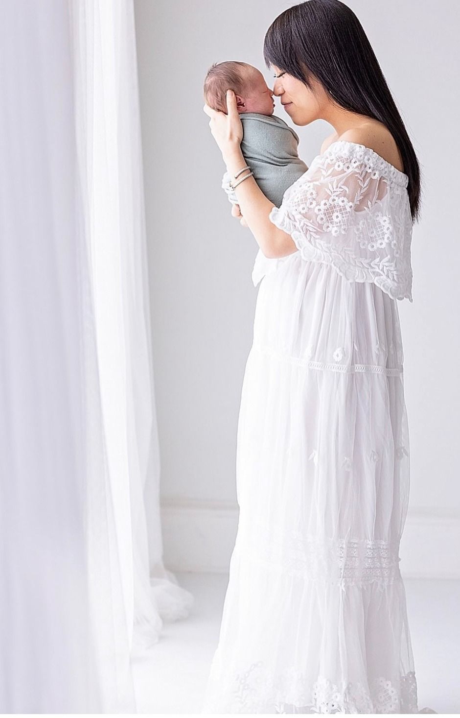Elegant maternity photos in a white lace dress against a bright studio background.