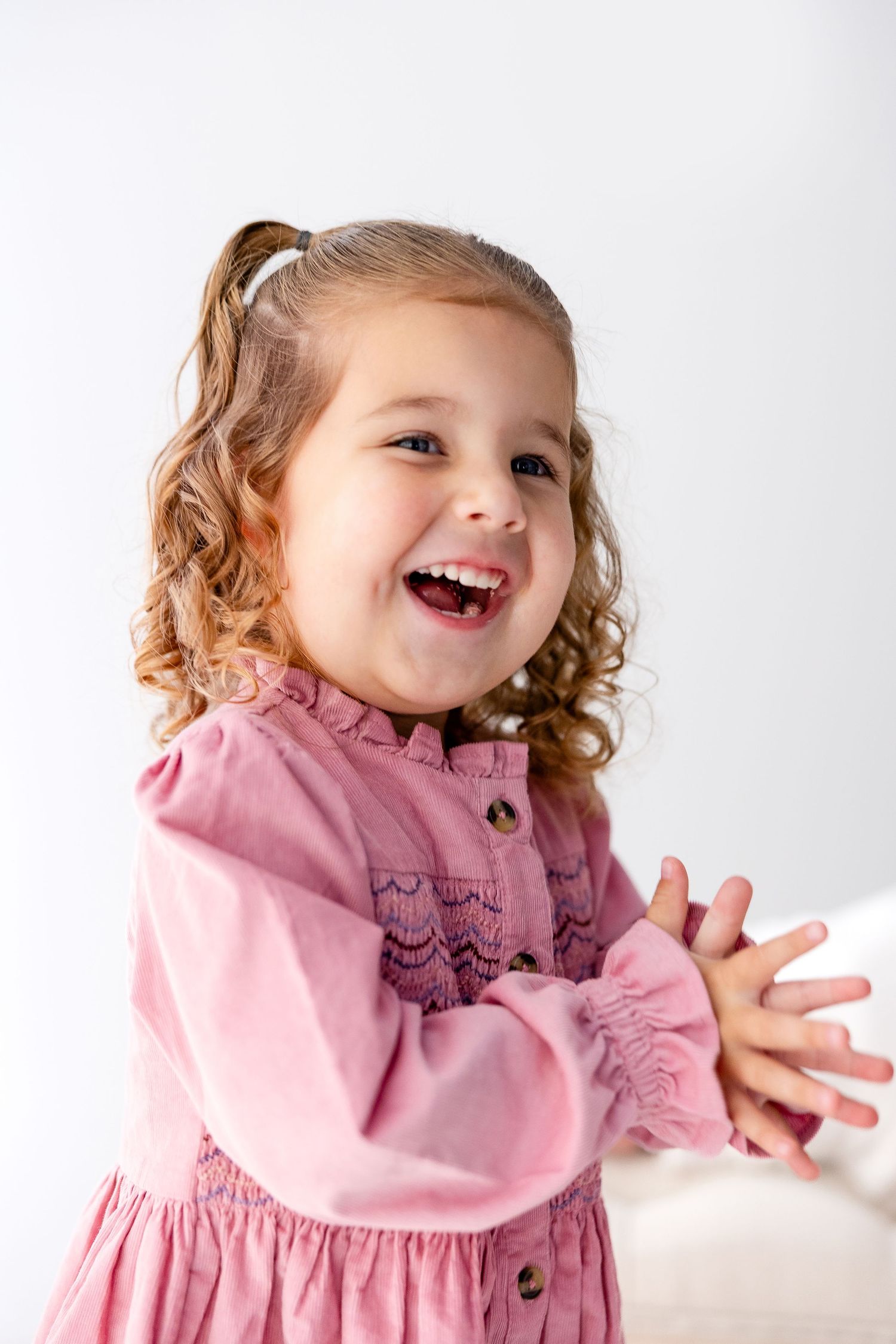 A toddler in a pink dress smiles and gestures playfully in a series of candid studio portraits.