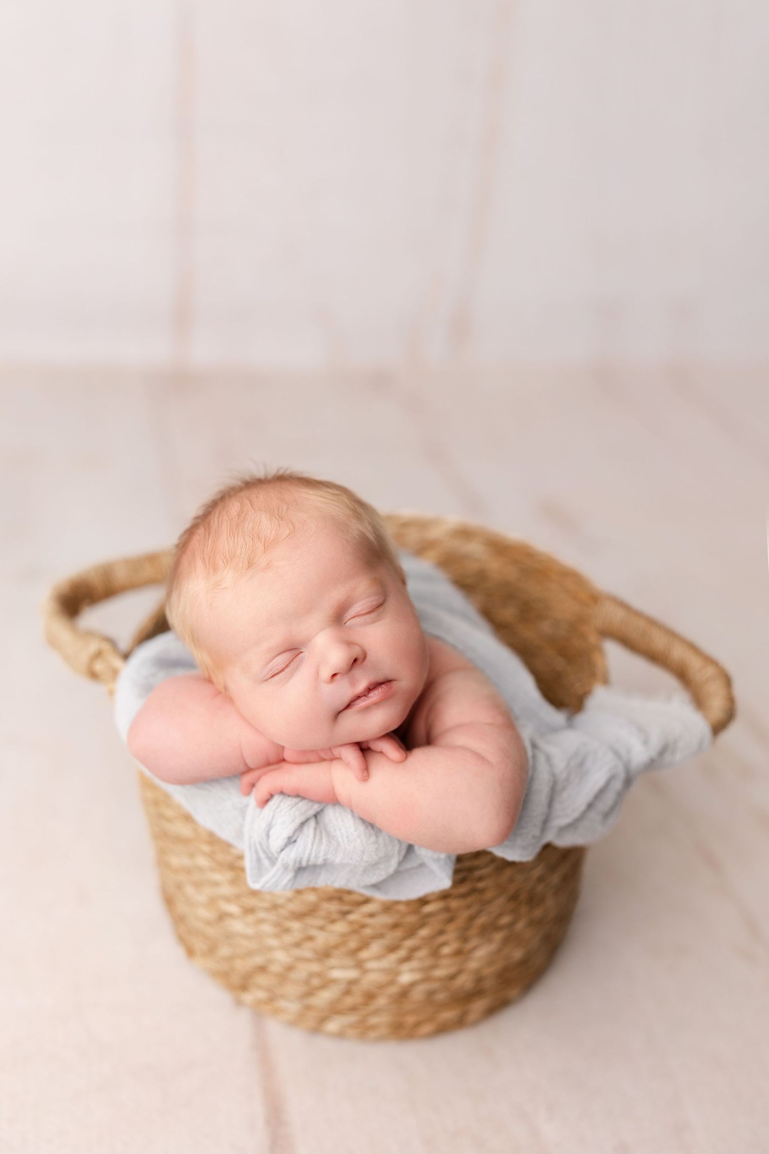 Peaceful sleeping newborn baby nestled in a woven basket with light blue wrapping.