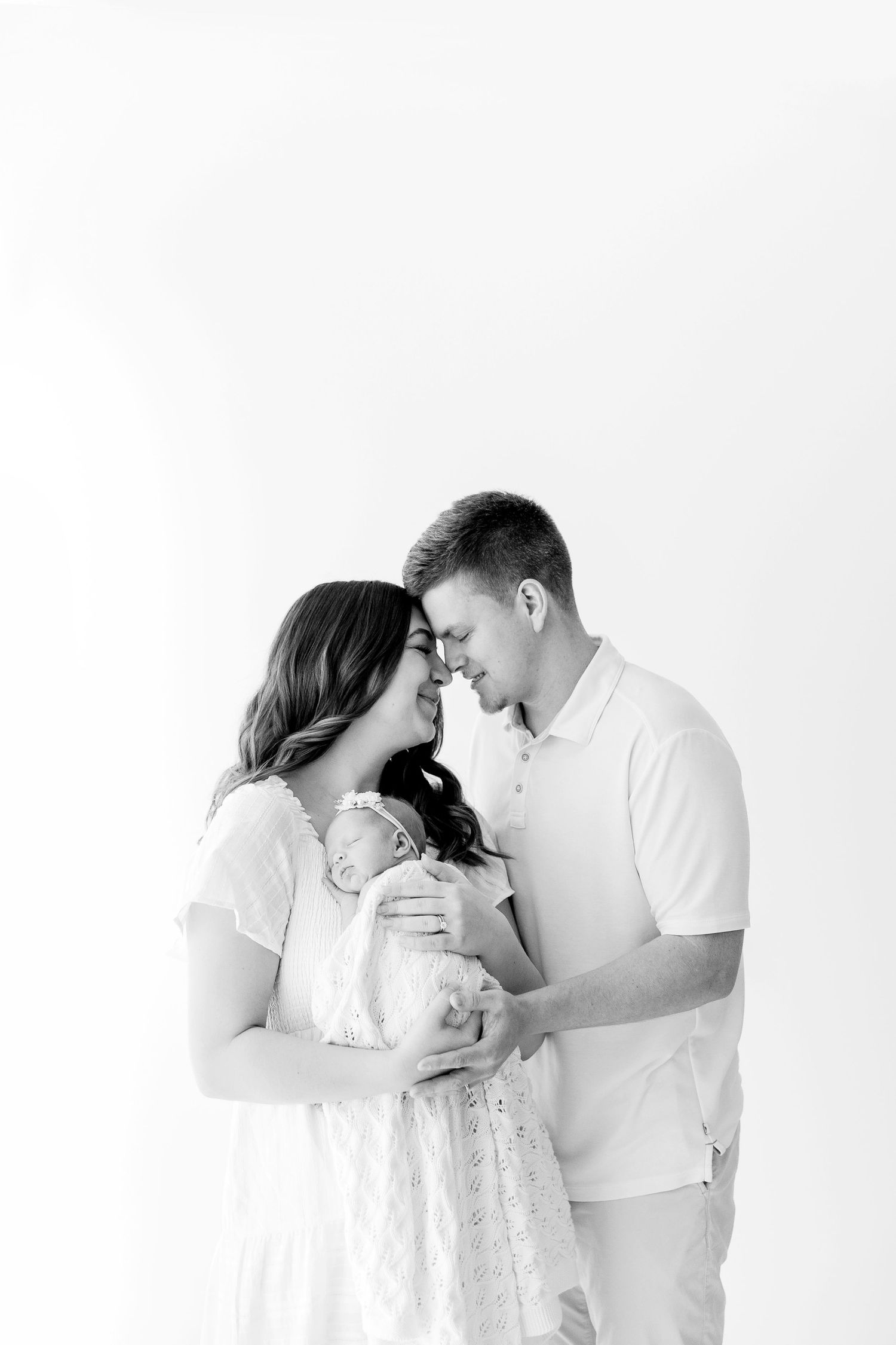 Intimate black and white portrait of family with newborn against white background.