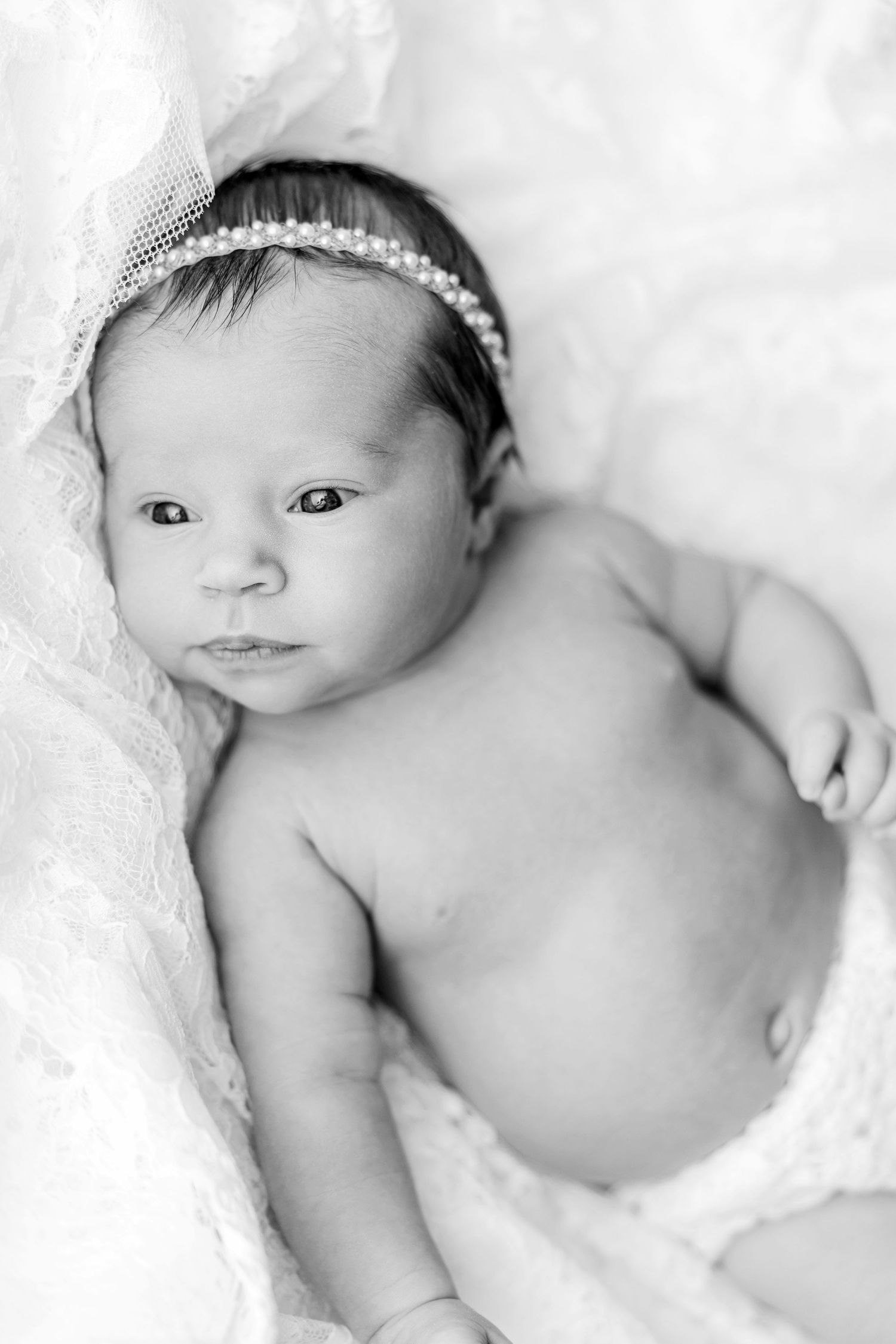 Black and white portrait of newborn wearing delicate headband on white blanket.