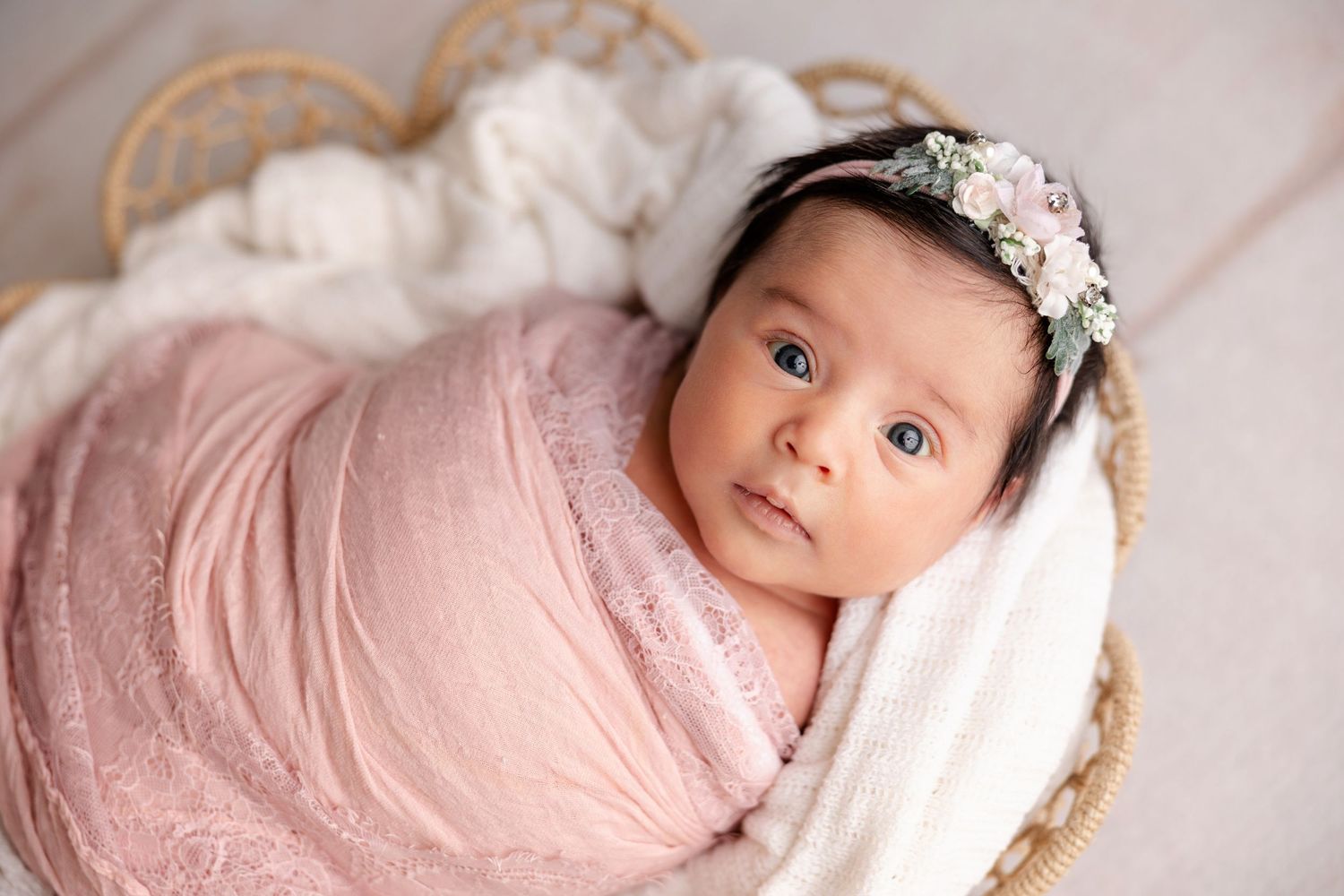 Newborn baby in pink wrap and floral headband poses during professional photography session.