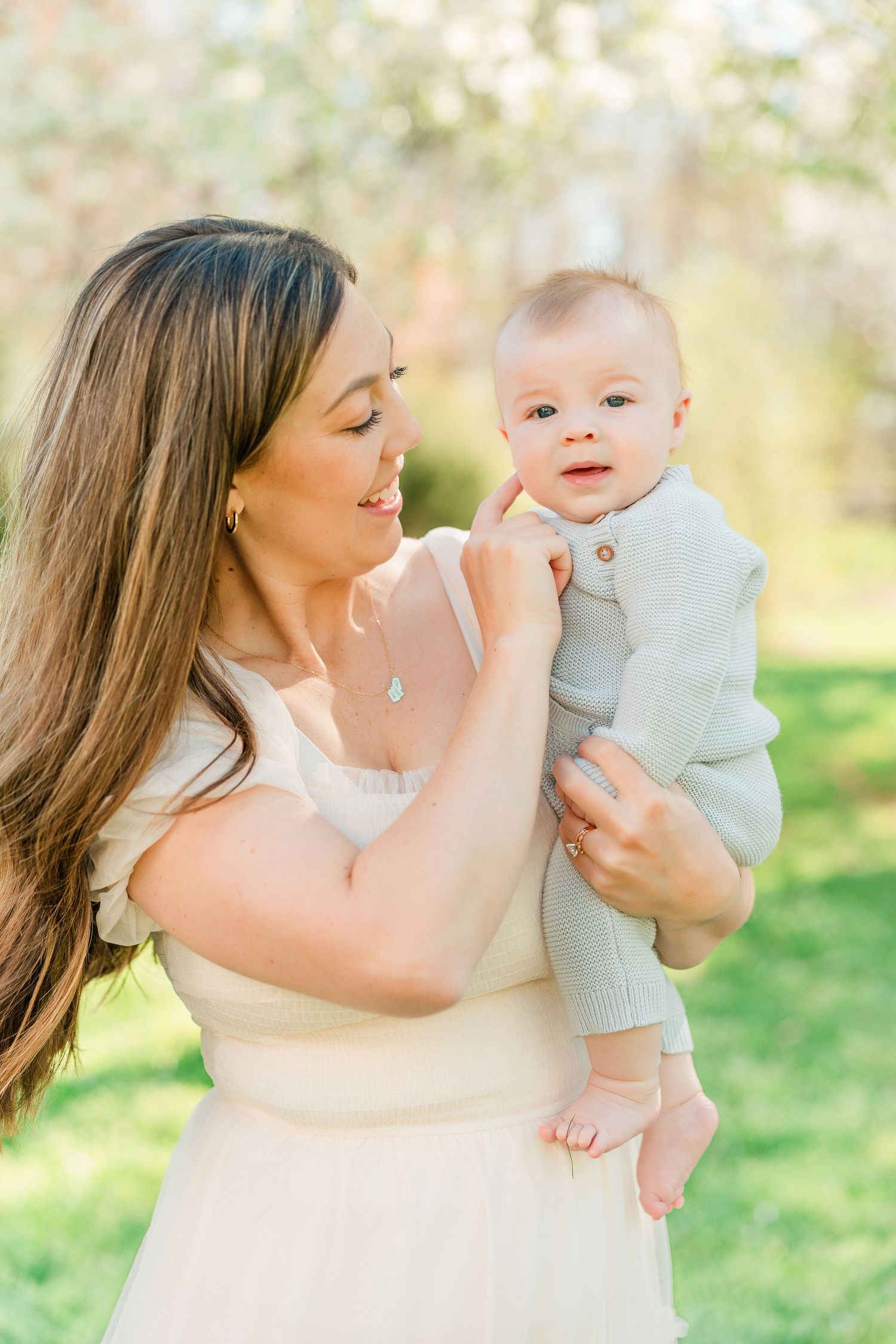 Mother and baby share joyful moments together in a sunlit garden setting with blooming trees.