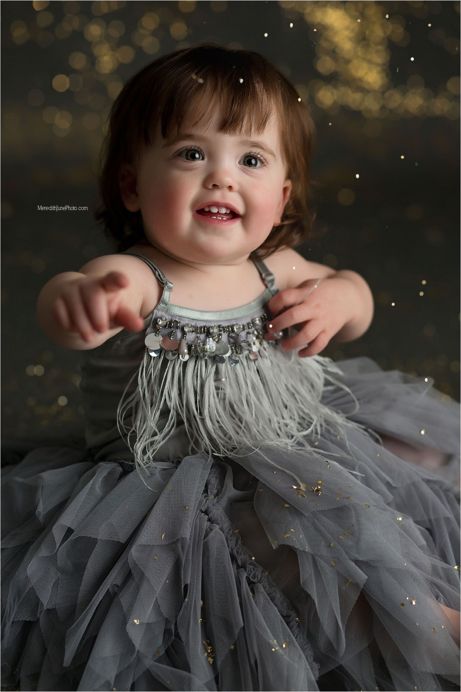 A grey tulle dress with sparkles catches the light during a festive photo session against a dark background.