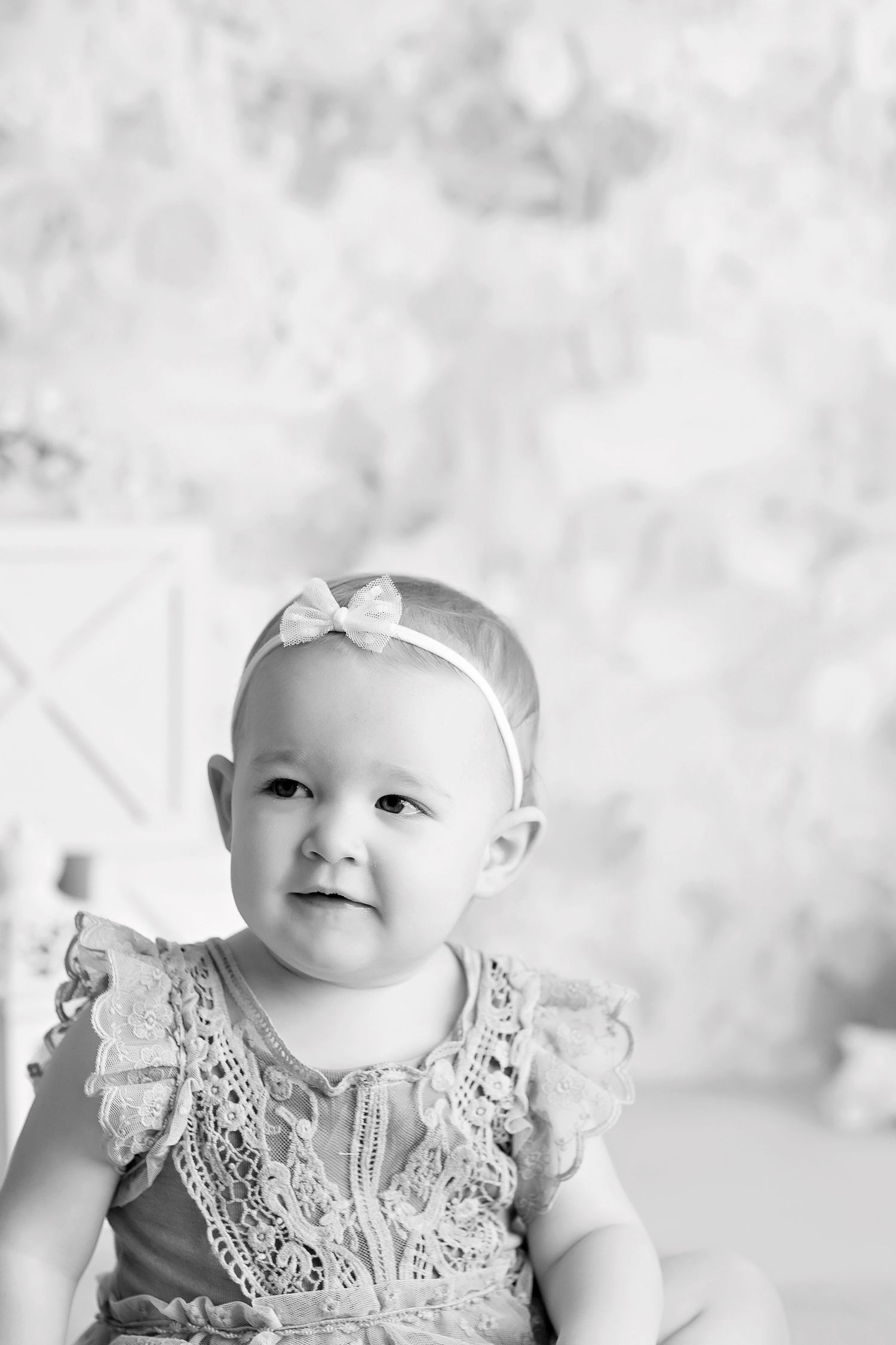A black and white portrait of a small child in a lace dress with a white headband.