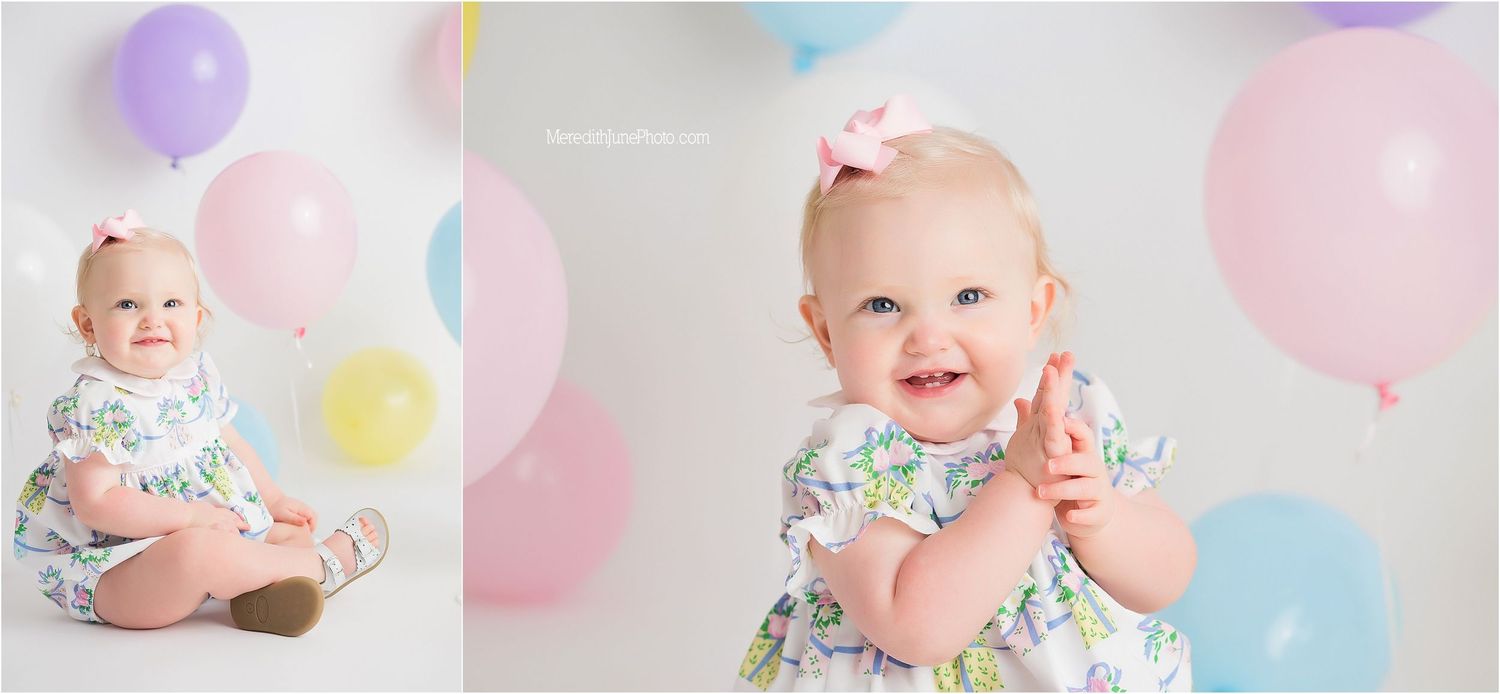 A baby in pastel surroundings smiles and plays with colorful balloons during a festive photo session.