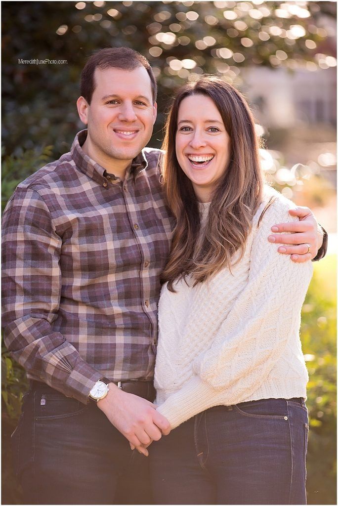 A couple embraces outdoors during a golden hour photo session wearing plaid and white sweater.