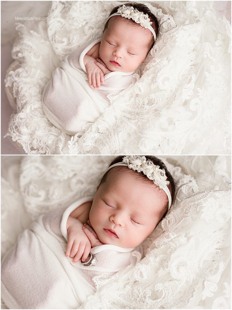 Newborn baby sleeping peacefully on white lace fabric wearing delicate headband and swaddled in soft white wrap.