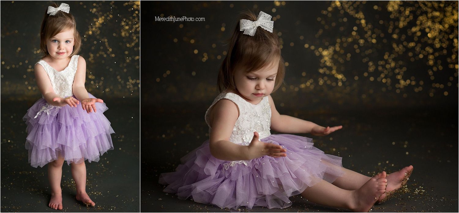 A small child in a purple tulle dress twirls and plays in a magical outdoor portrait session with glittering lights.
