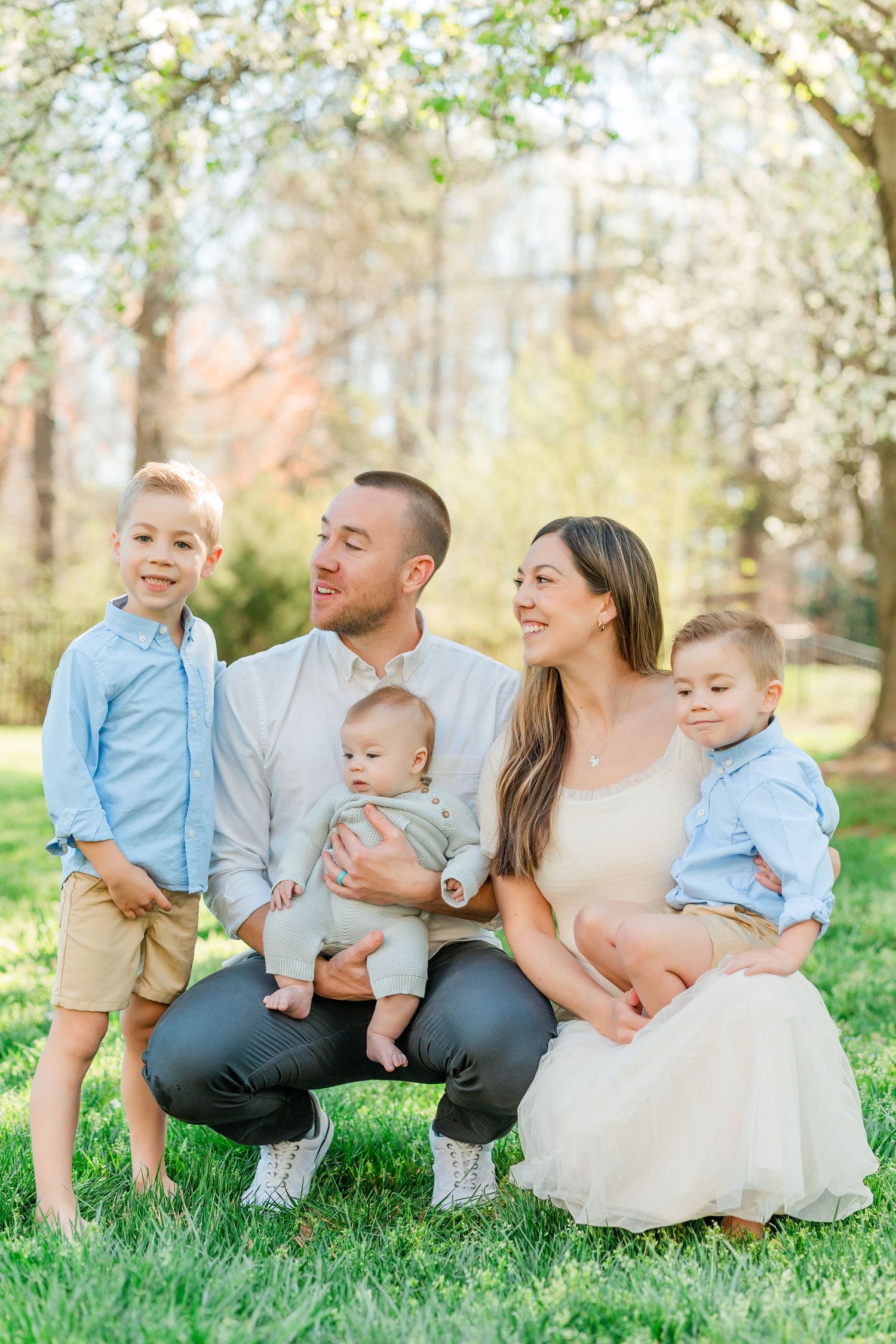 Family sitting together on grass during spring with blooming trees in background.