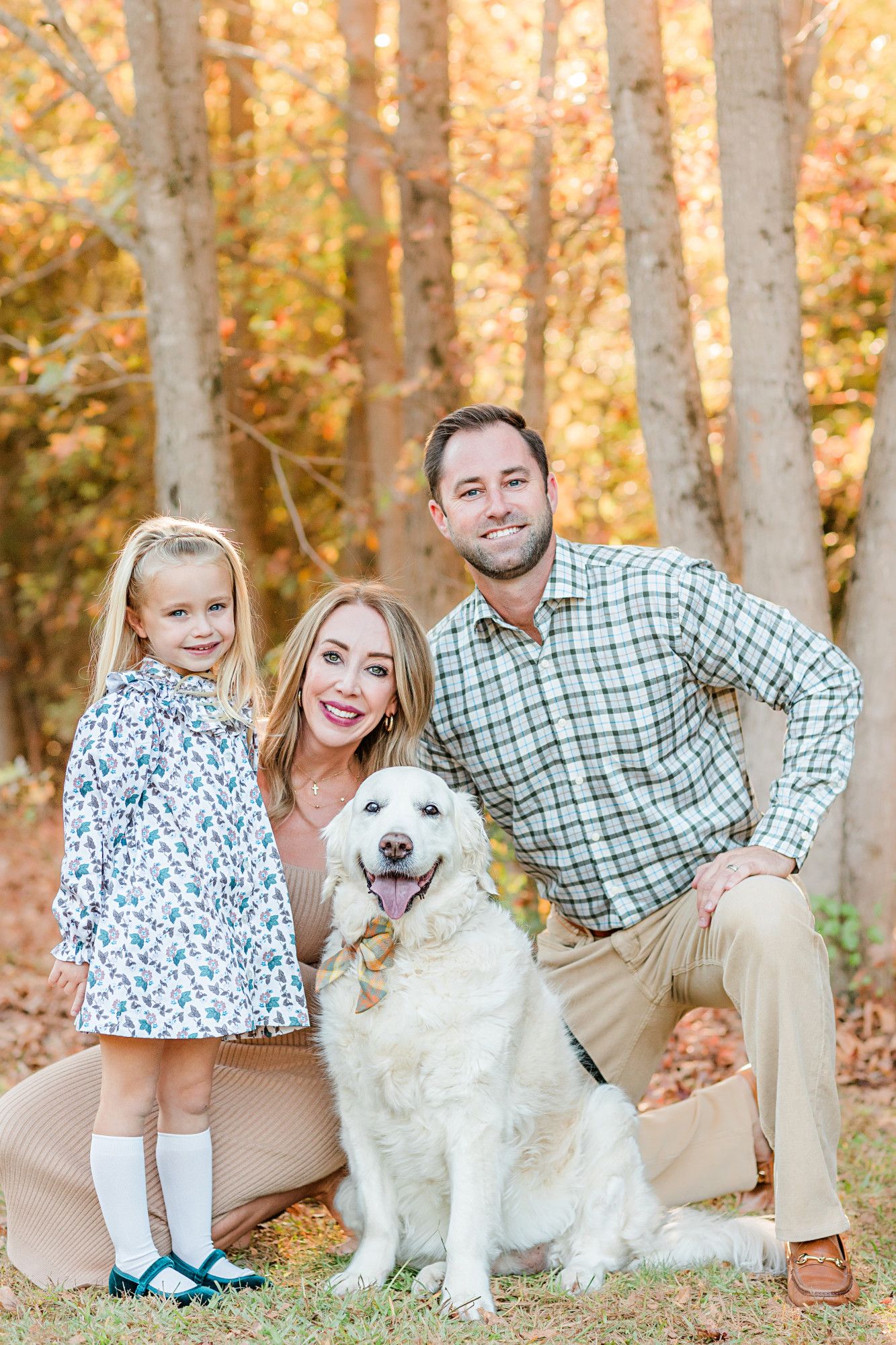 Happy family with white dog posing together in autumn forest setting.