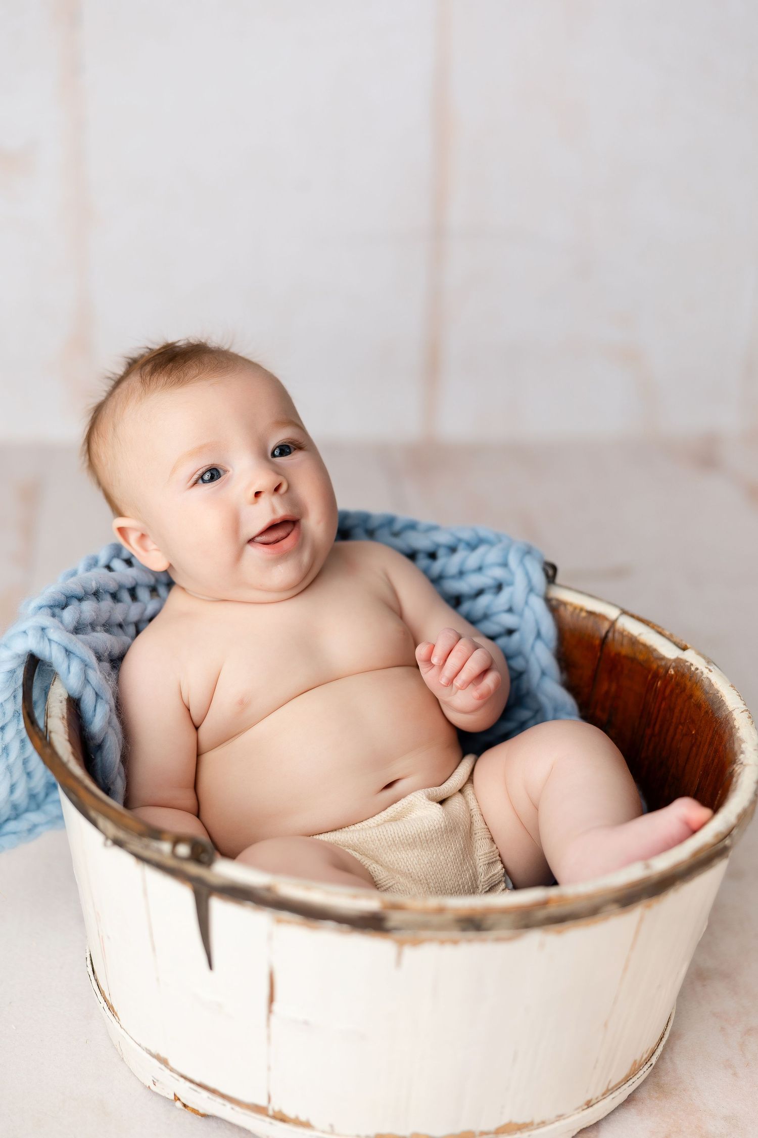 A happy baby lying in a rustic white wooden basket with a soft blue blanket.
