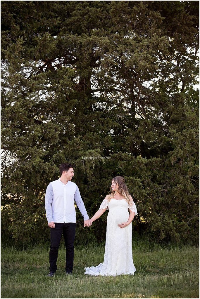 Romantic outdoor wedding photos of couple walking through a green field at sunset with trees in background.