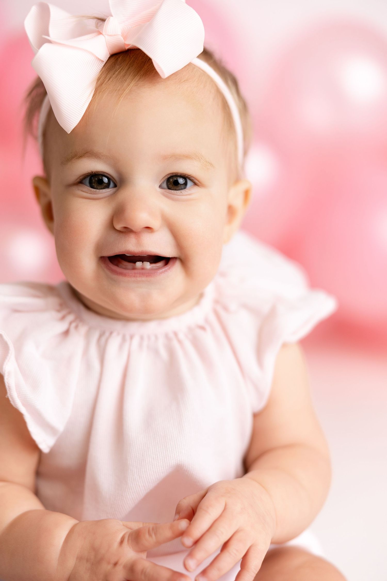 Baby wearing white ruffled dress and bow smiles sweetly in pink-toned portrait photography collage.