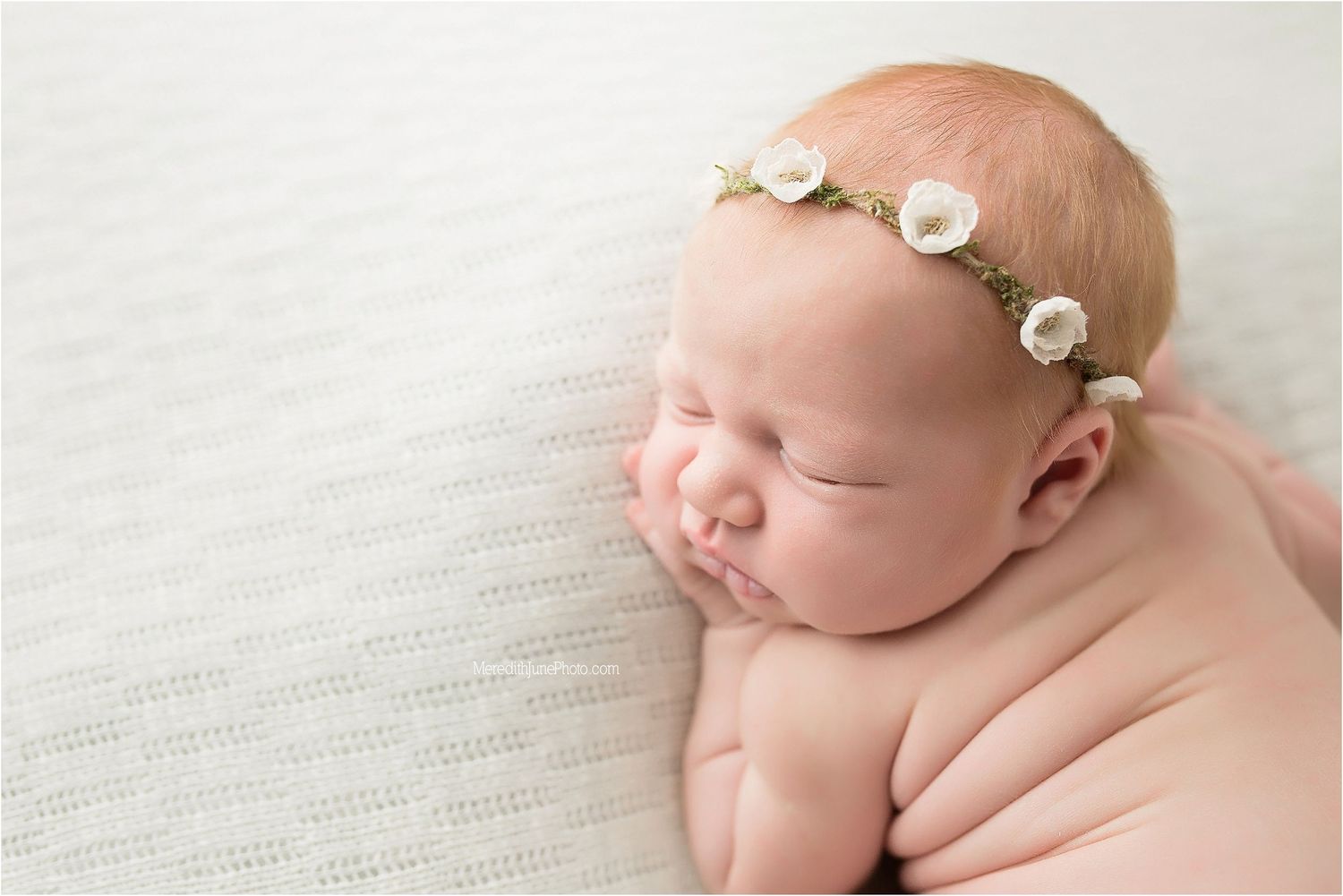 Newborn baby sleeping peacefully on soft white blanket with delicate floral headband.