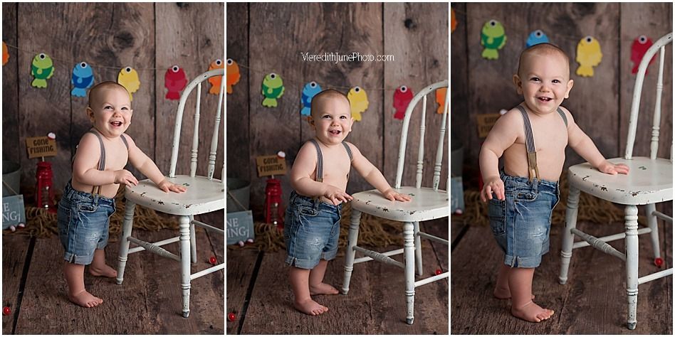 A baby in denim overalls plays with a white chair during a first birthday cake smash photo session.