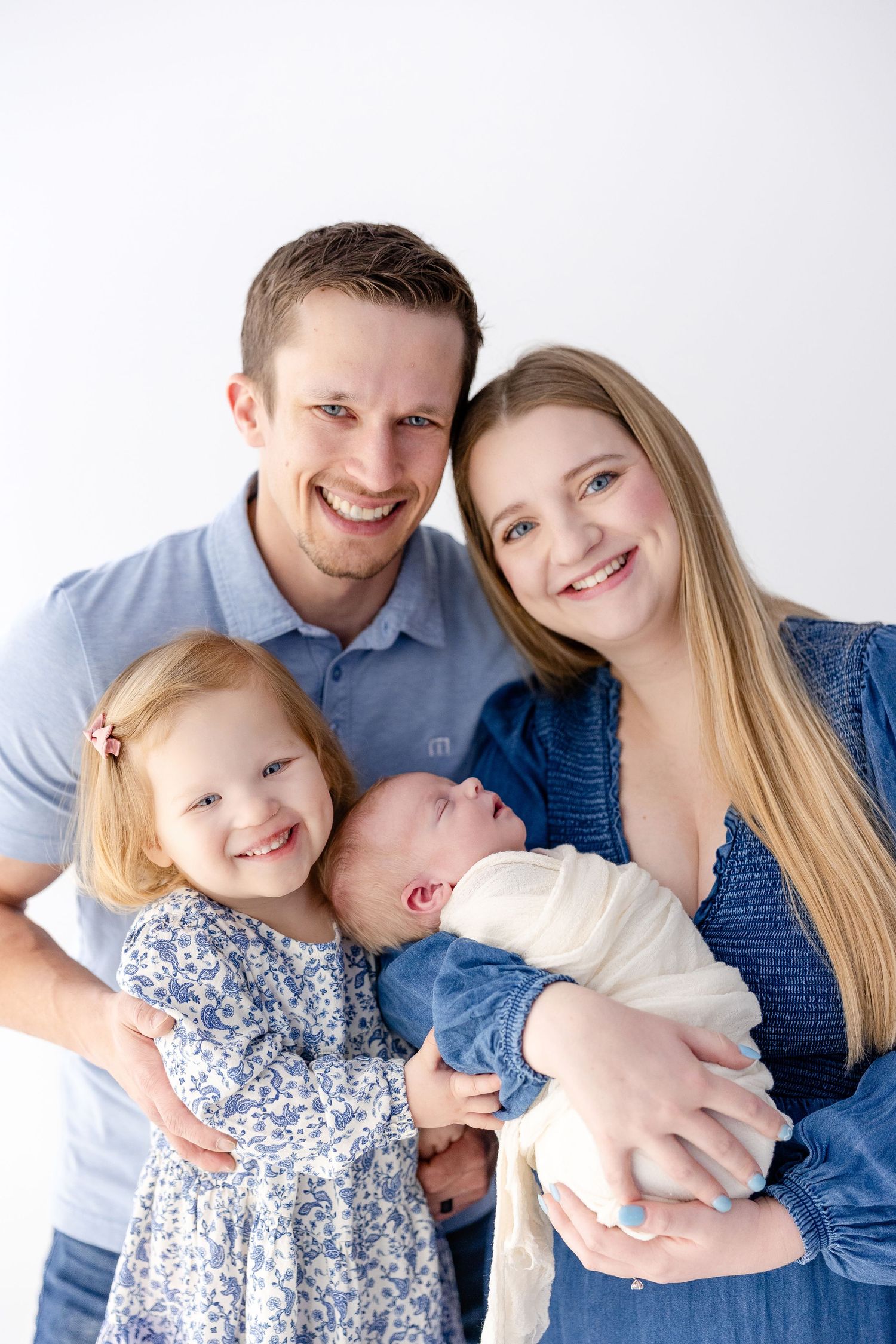 Happy family portrait against white background showing parents with two young children.