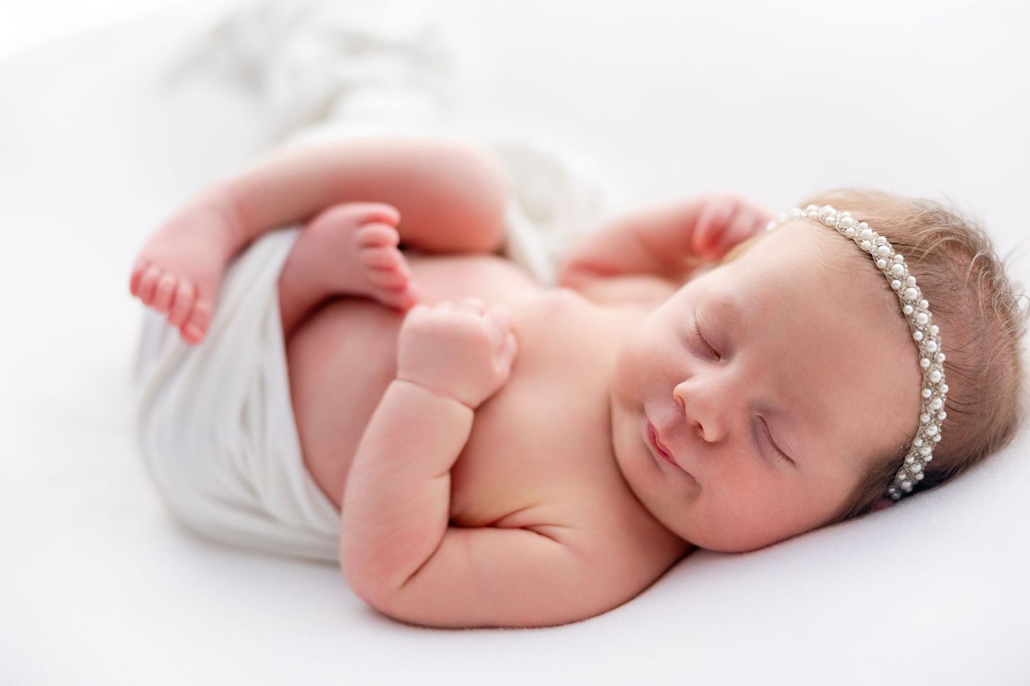 A sleeping newborn baby wearing a delicate headband lies peacefully on white bedding in four different poses.