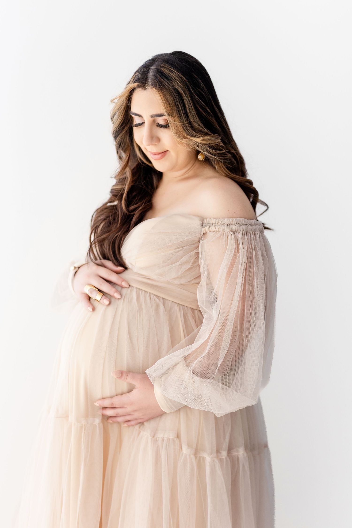 Woman in flowing peach dress poses gracefully against white backdrop.