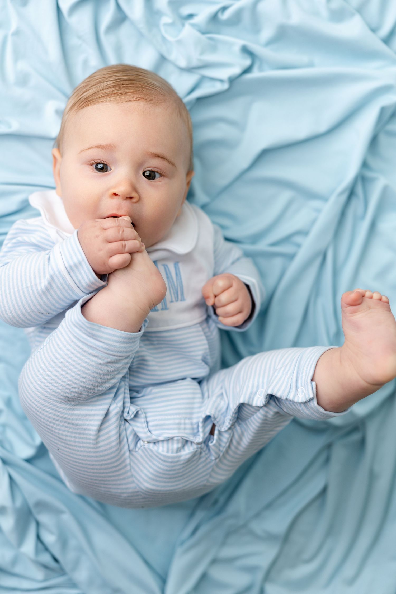 Baby wearing blue and white striped outfit lying on light blue bedding in a series of playful poses.