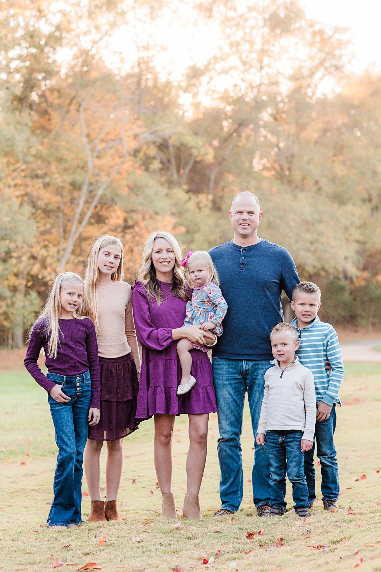Family group wearing coordinated purple and blue outfits posing outdoors in autumn setting.