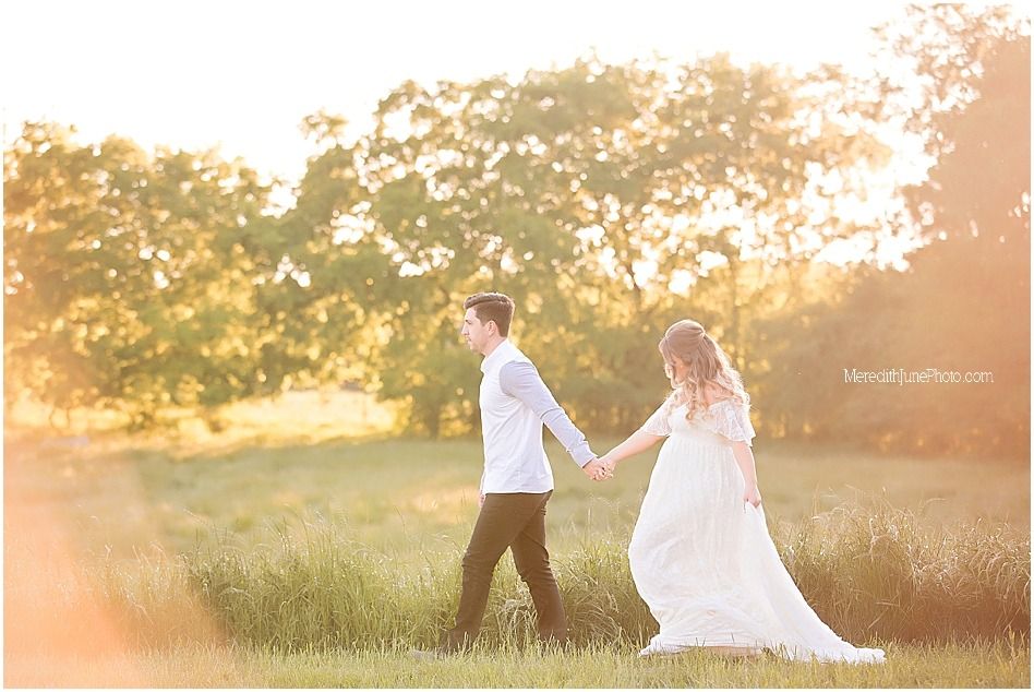A romantic couple in wedding attire dances together in a sunlit field during golden hour.