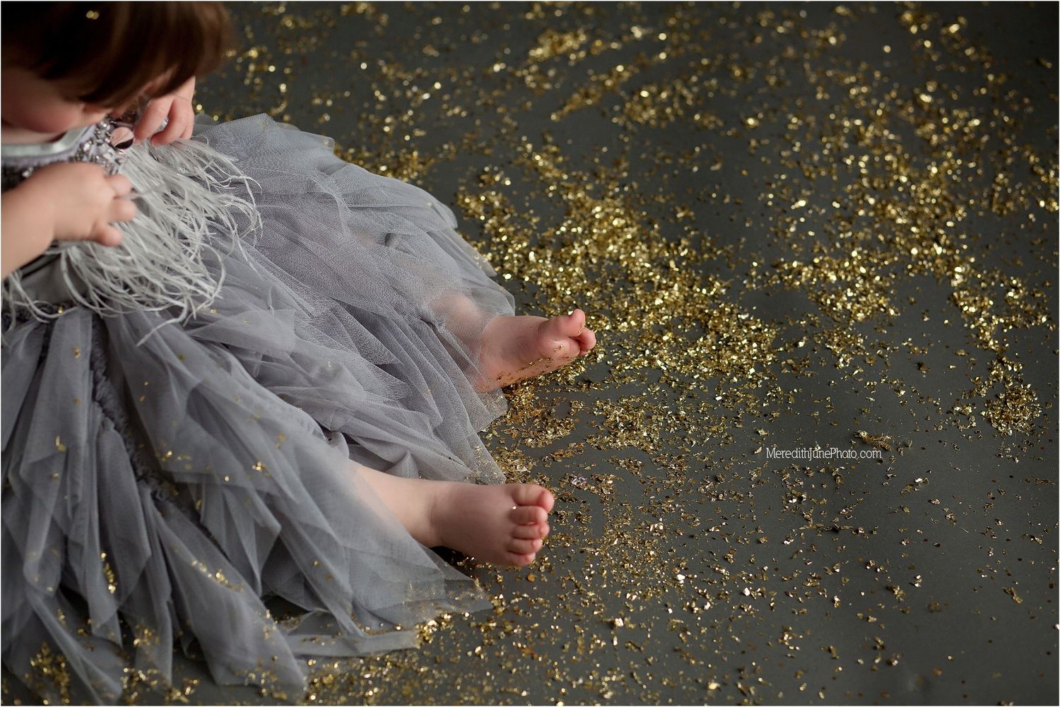 Glittery gold confetti falls around a flowing gray dress against a dark background.