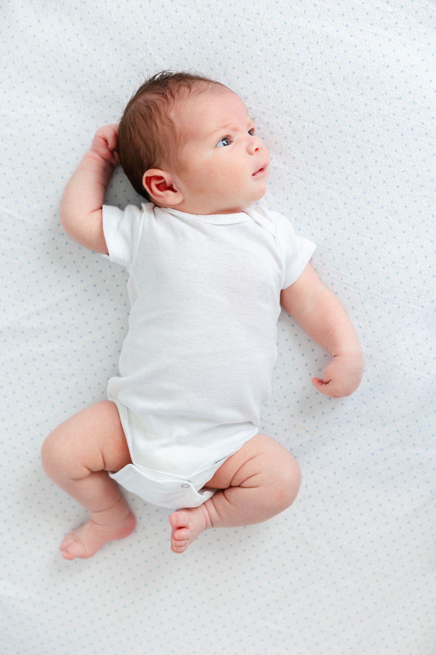 Newborn baby wearing white onesie photographed from different angles on light background.