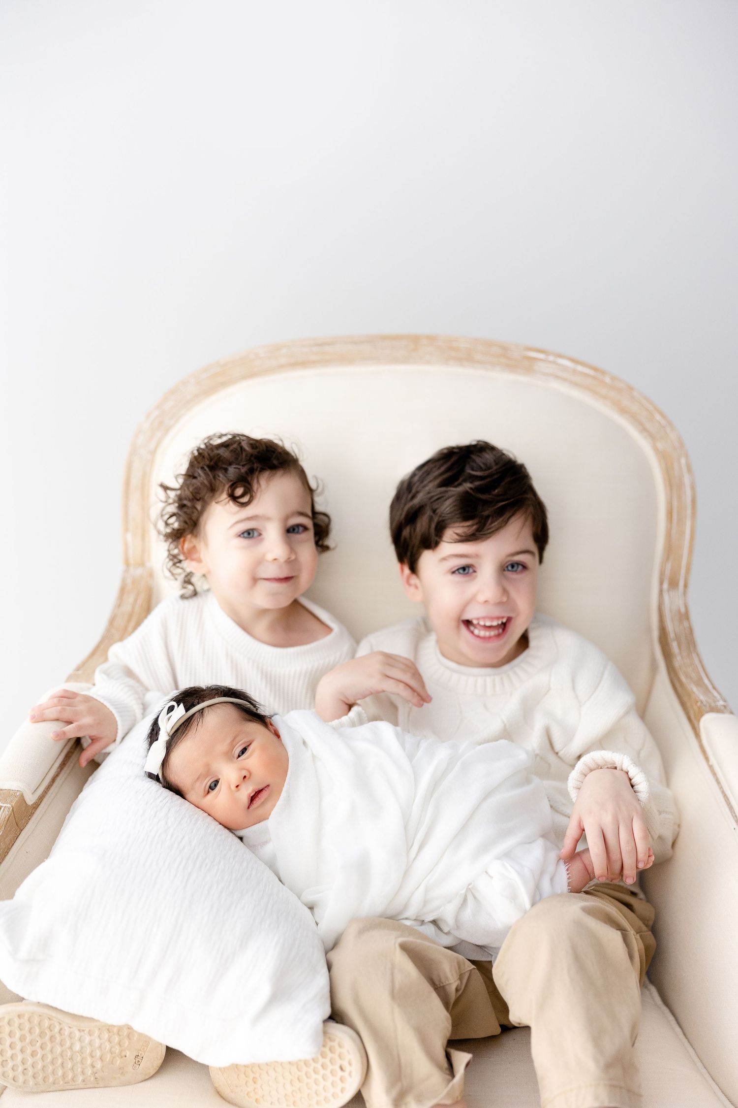 Three connected photos show children in white tops and beige pants playing and laughing together on a light colored couch.