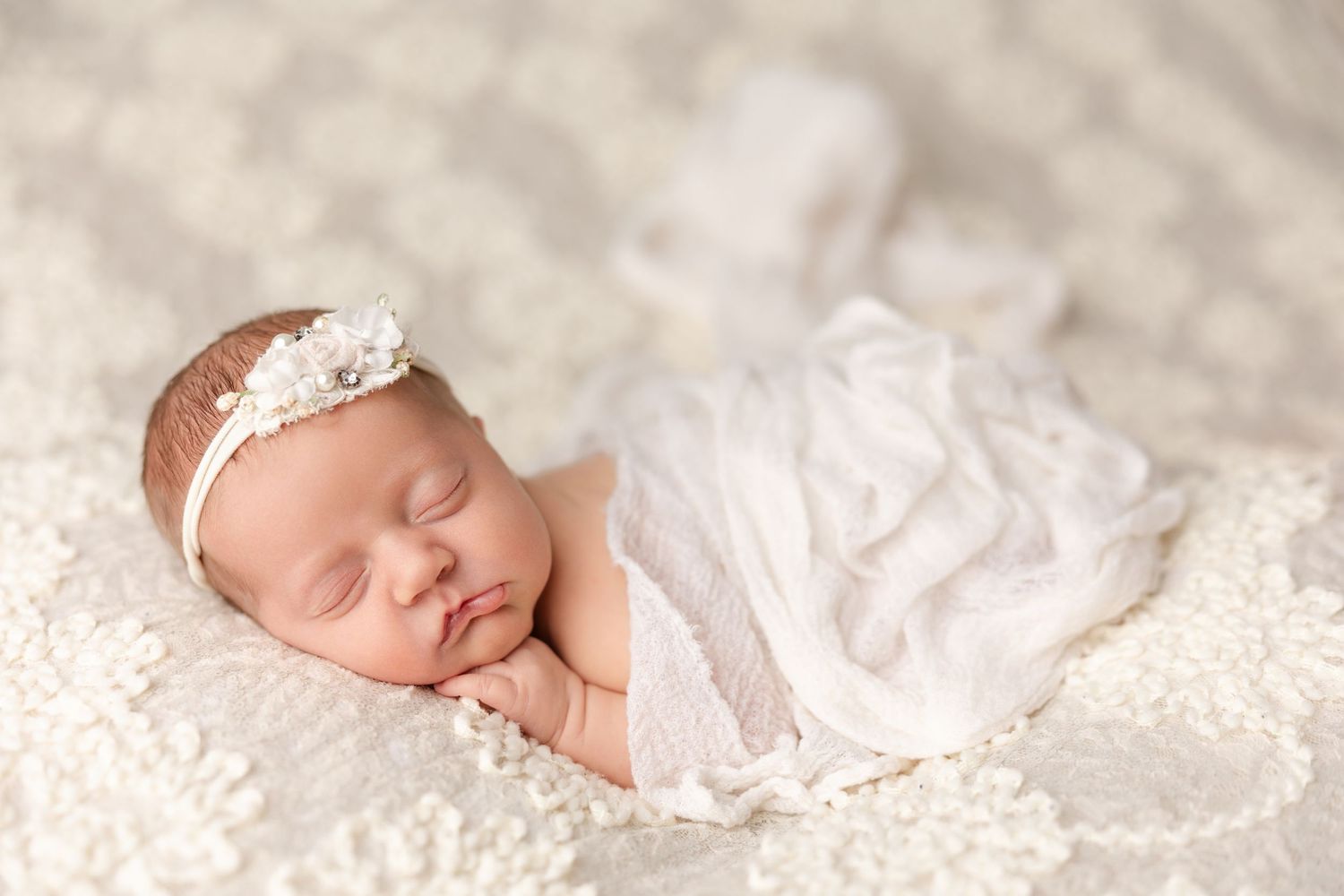 Sleeping newborn baby wrapped in delicate white lace fabric during professional portrait session.