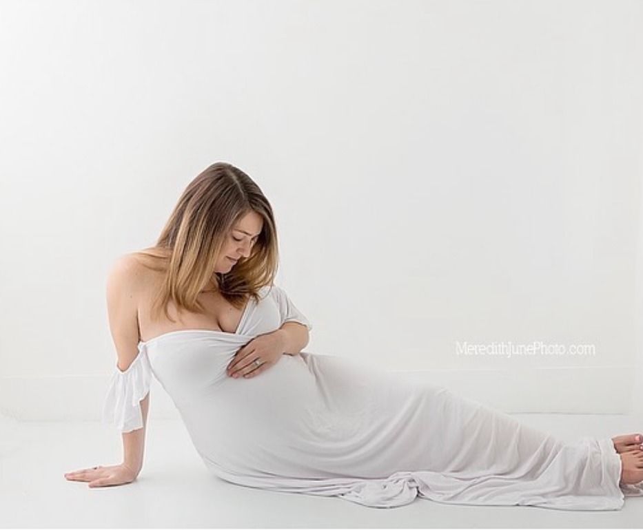 A person in white loungewear stretches gracefully on a light colored floor in a minimalist setting.