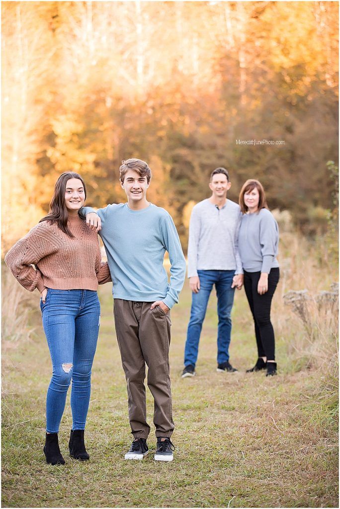 Family group poses playfully in a golden autumn field with warm sunlit foliage in the background.