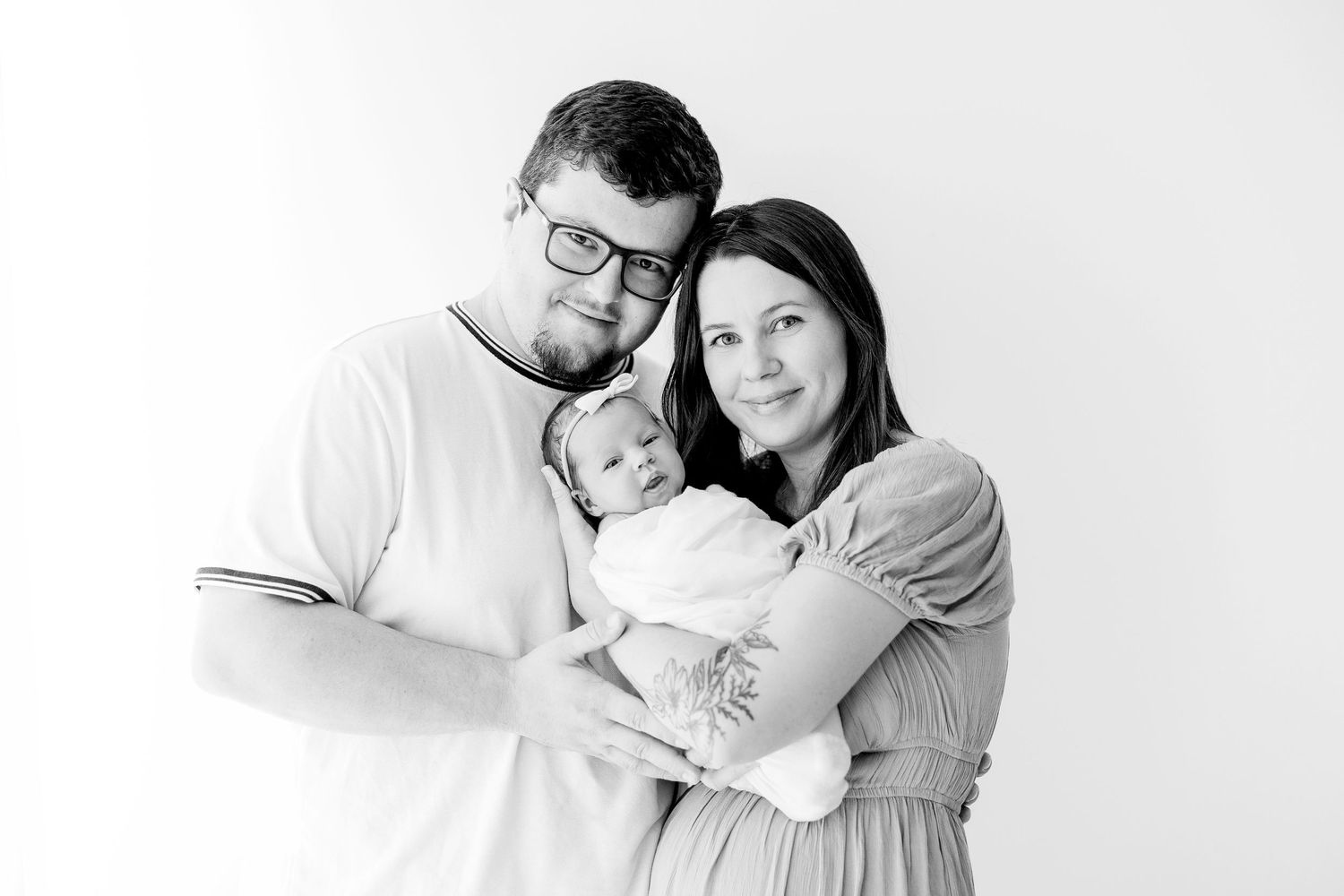 Family portrait in white clothing against neutral background showing tender embrace.