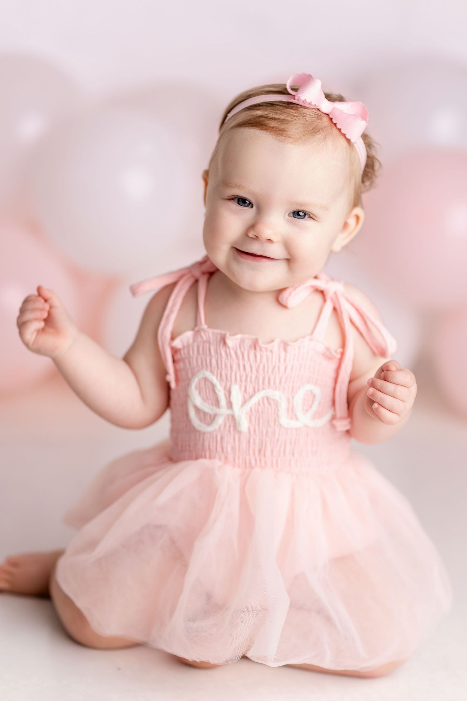 Baby in pink dress smiles and poses during studio photo session.