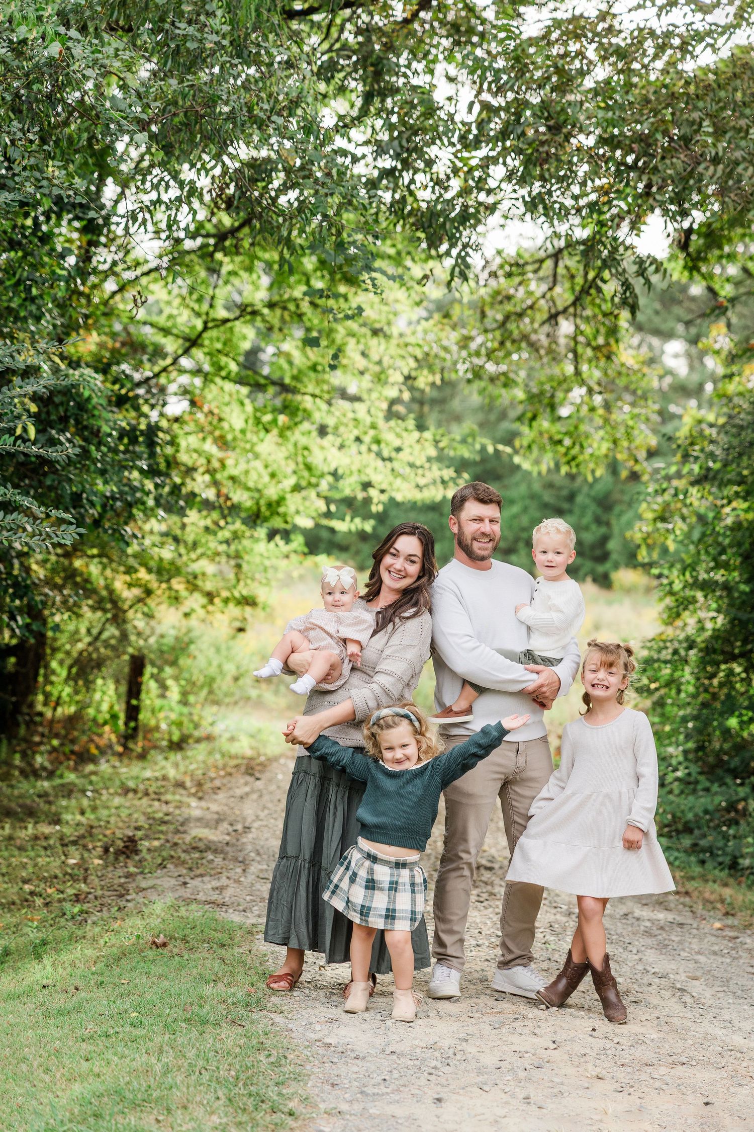 Family enjoying playful moments together on a tree-lined outdoor path.