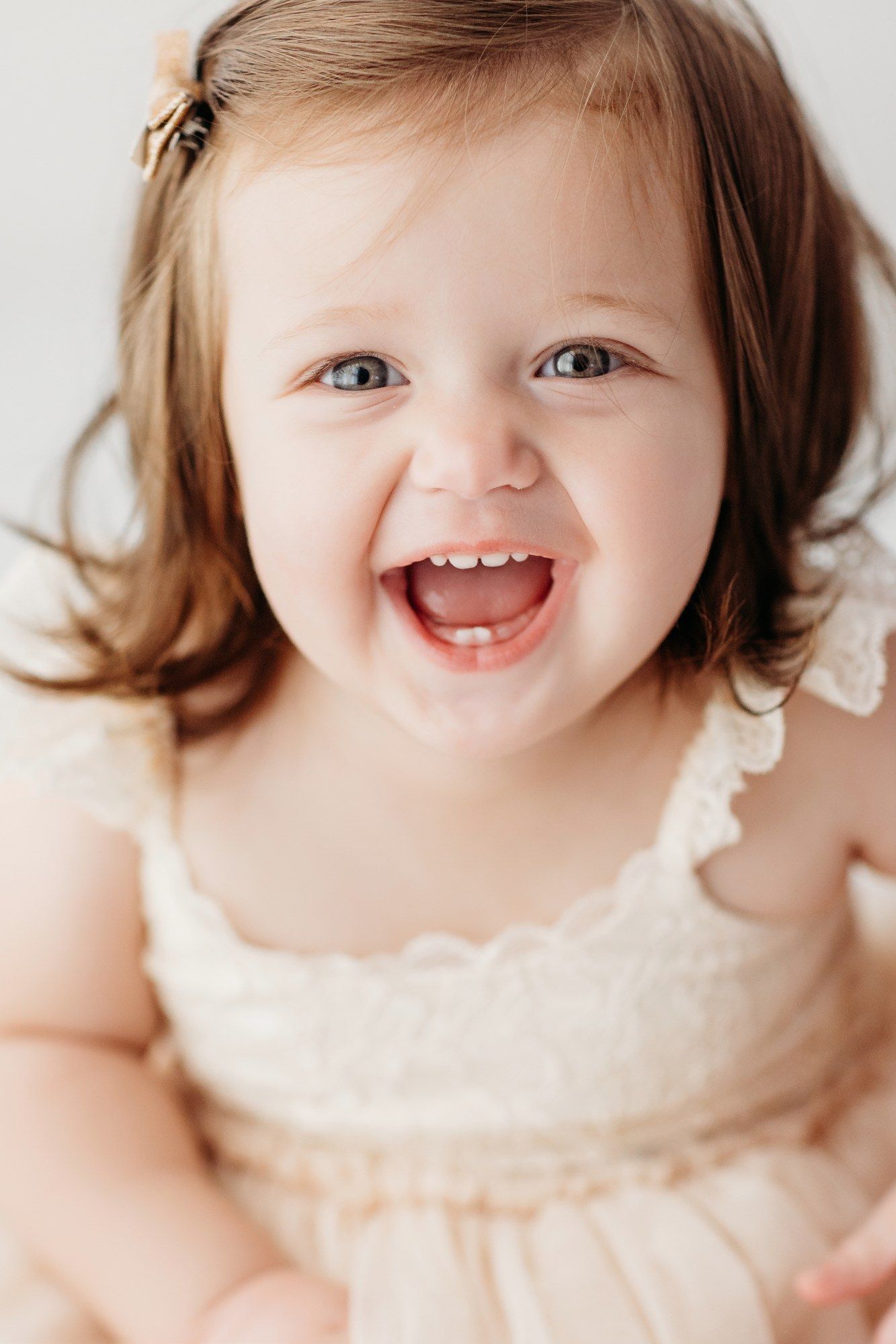 Toddler in cream dress laughing joyfully during portrait session.