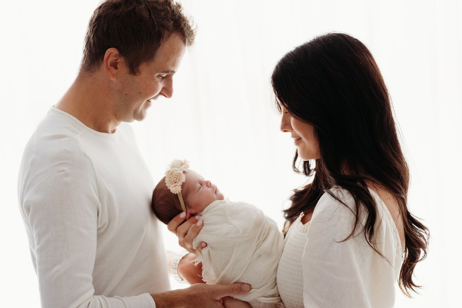 Intimate family portrait series with newborn baby in white studio setting.