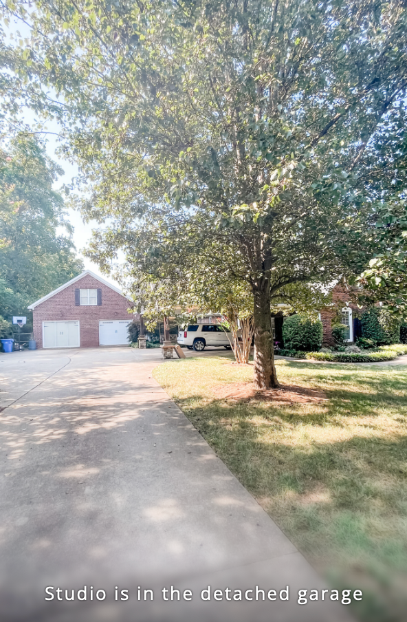 A tree-lined gravel driveway leads to a detached red brick garage in a rural setting.