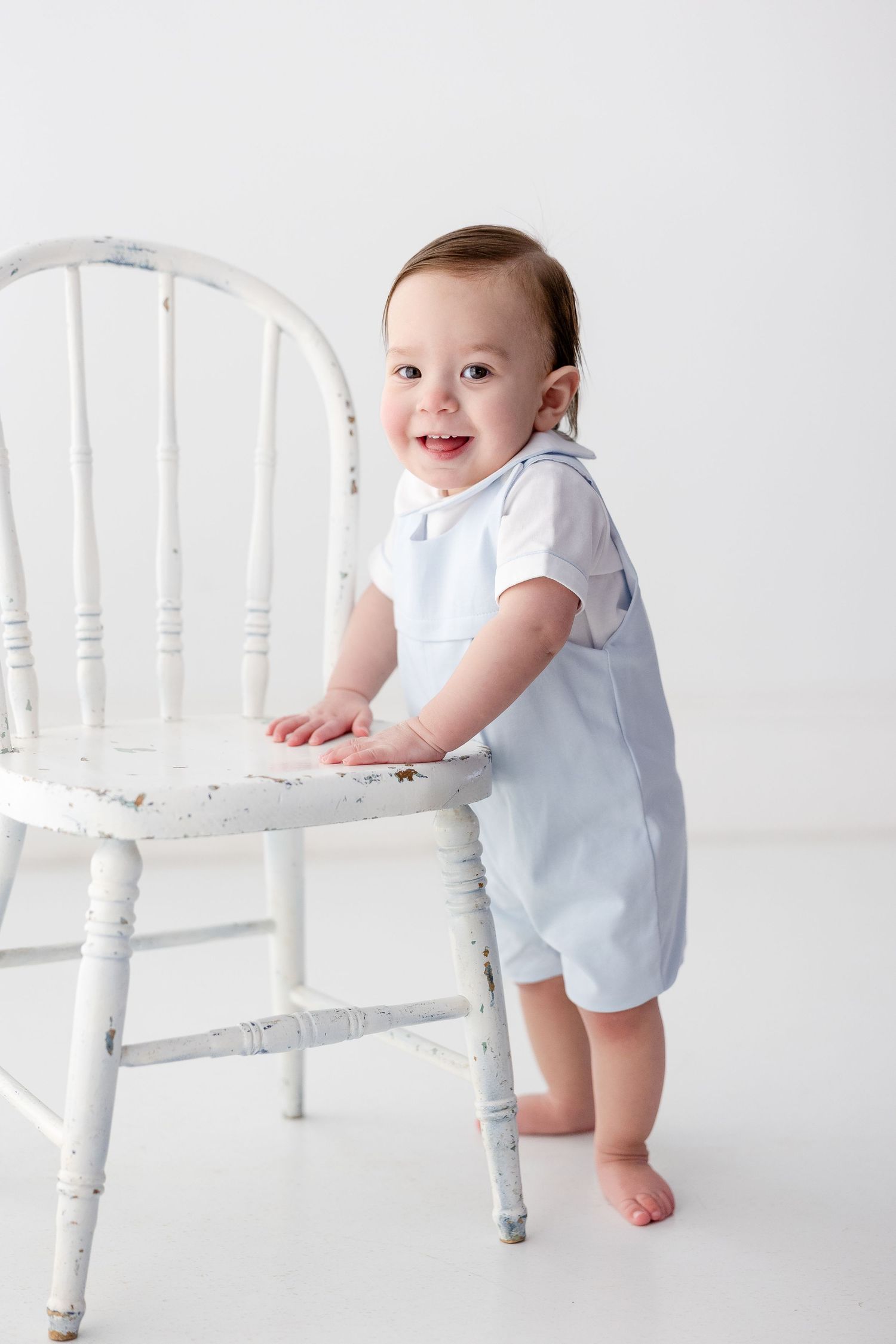 Three sequential photos show a baby in a light blue outfit standing and holding onto a white vintage-style chair.