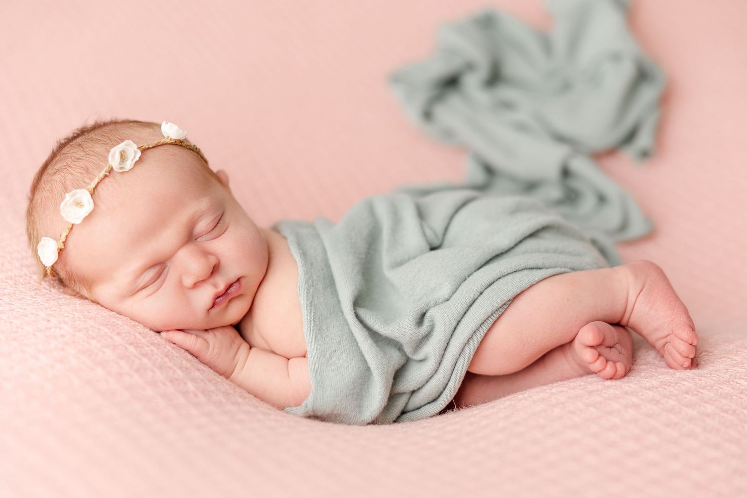 Peaceful sleeping newborn wrapped in soft mint green fabric lying on pink textured background.