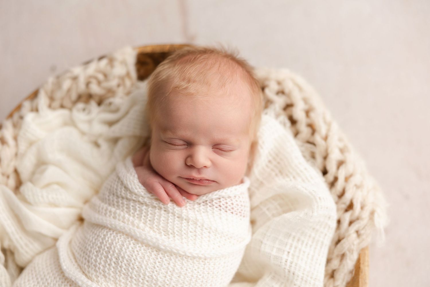 A sleeping newborn baby swaddled in soft white blankets rests peacefully during a professional photo session.