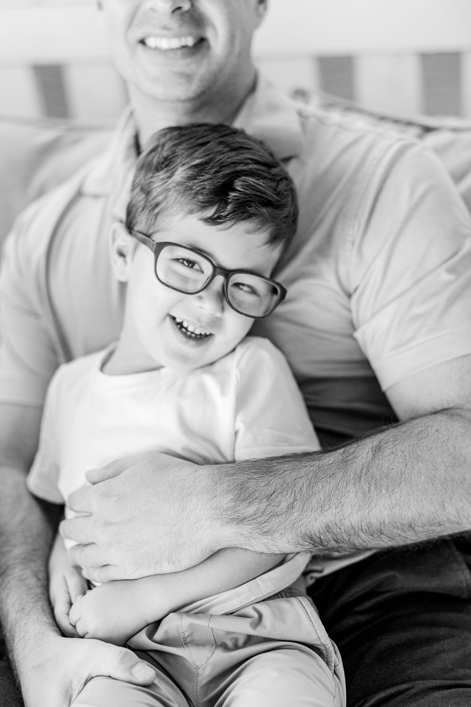 Black and white candid photos show a child wearing glasses laughing while relaxing on a couch.