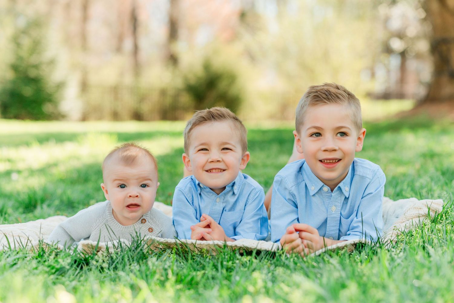 Children wearing matching blue shirts lying on grass during an outdoor photo session in a sunny park.