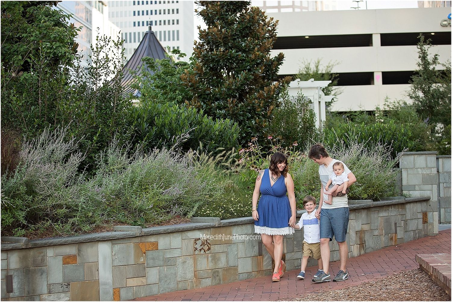 People walking together along a stone wall path with lush gardens and urban buildings in the background.