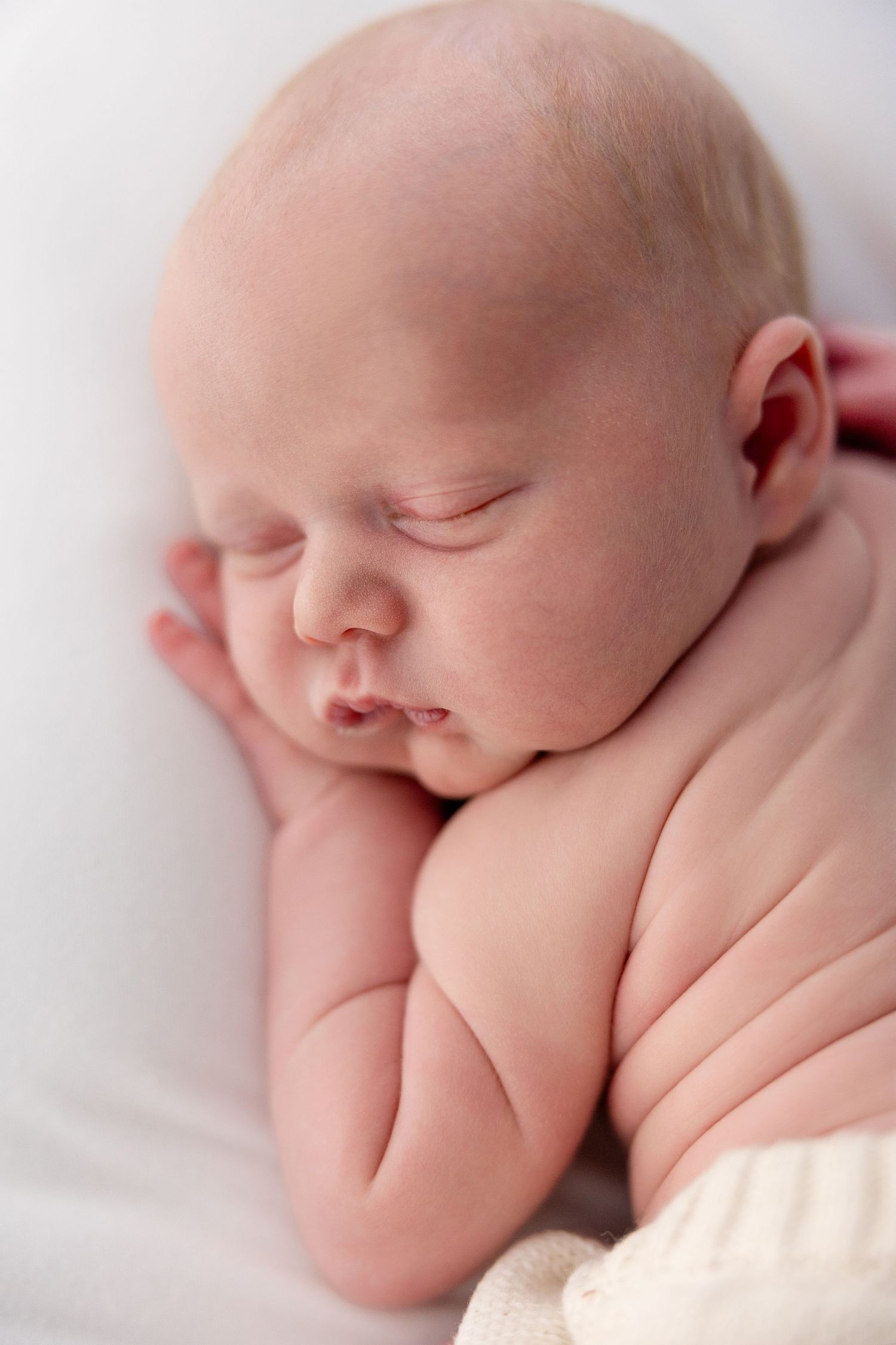 Peaceful sleeping newborn baby with chubby cheeks resting on tiny hands against white background.