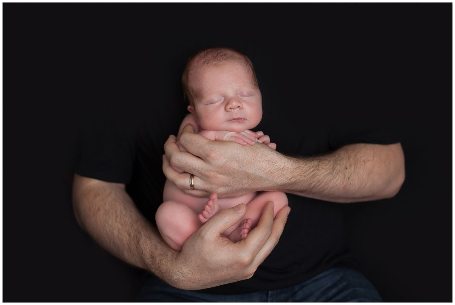 Gentle hands cradling a sleeping newborn against a black background in artistic black and white portraits.